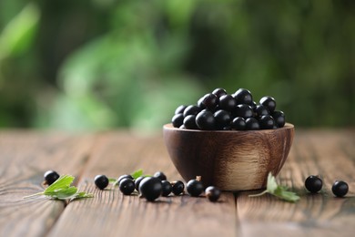 Photo of Ripe black currants and leaves in bowl on wooden table, space for text