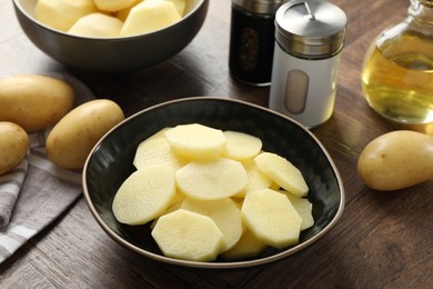 Photo of Fresh raw potatoes, spices and oil on wooden table