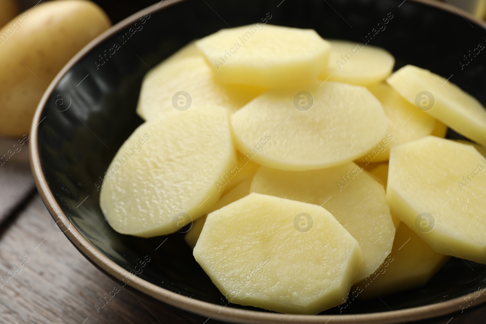 Photo of Cut fresh raw potatoes in bowl on wooden table, closeup