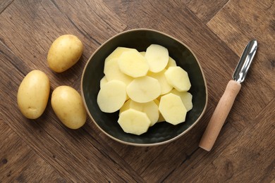 Photo of Fresh raw potatoes and peeler on wooden table, top view