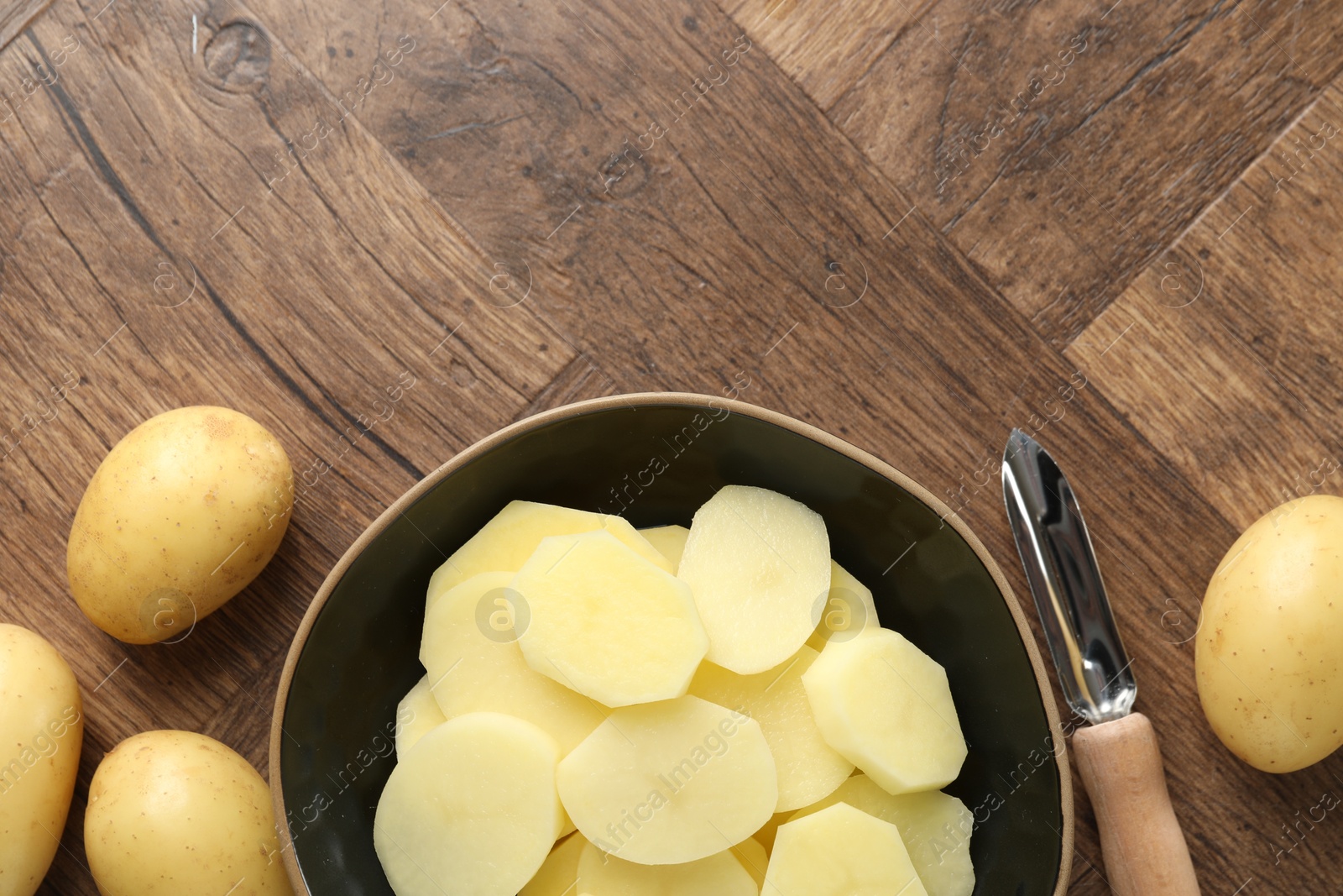 Photo of Fresh raw potatoes and peeler on wooden table, top view. Space for text