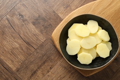 Cut fresh raw potatoes in bowl on wooden table, top view. Space for text