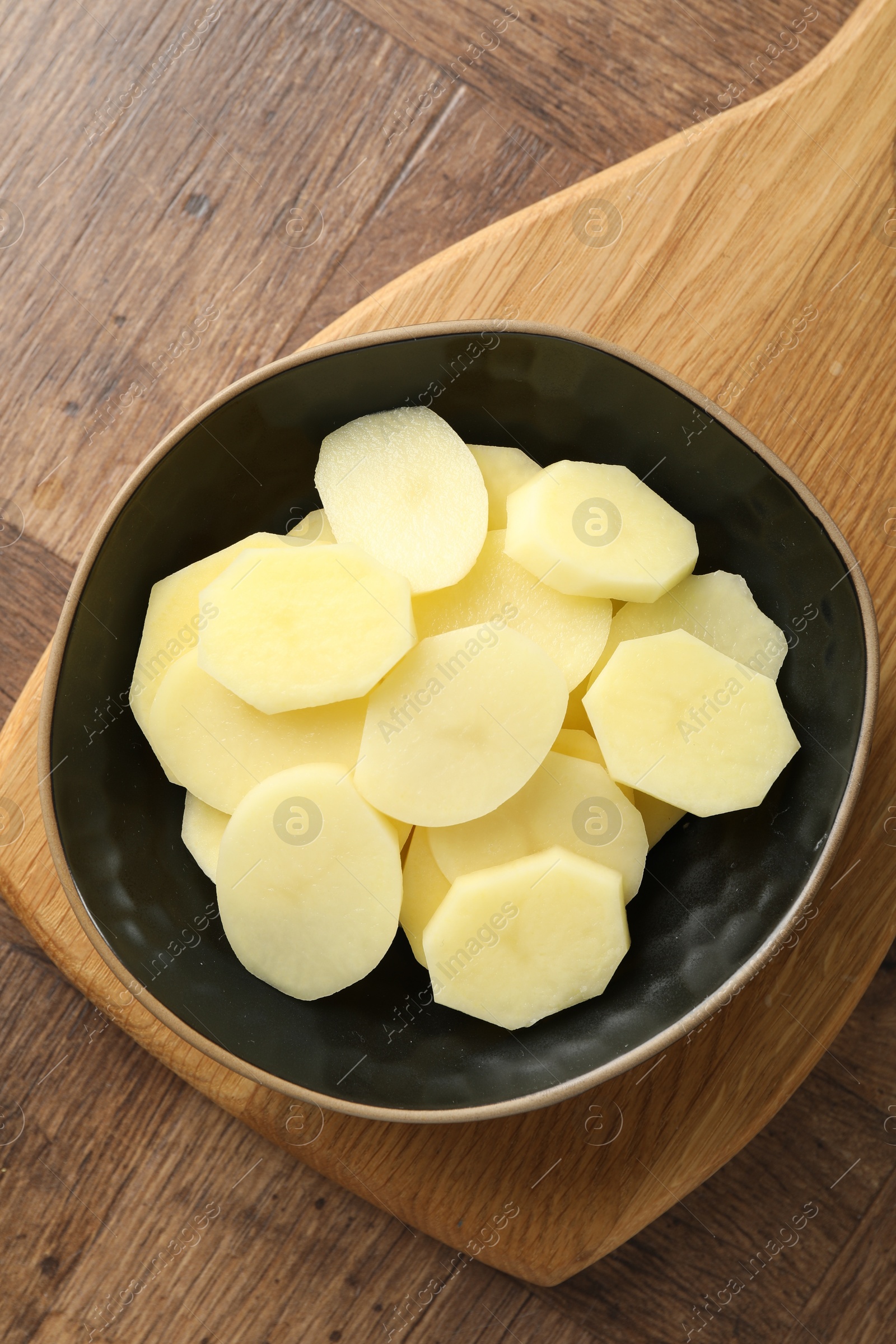 Photo of Cut fresh raw potatoes in bowl on wooden table, top view