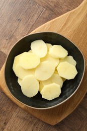 Photo of Cut fresh raw potatoes in bowl on wooden table, top view