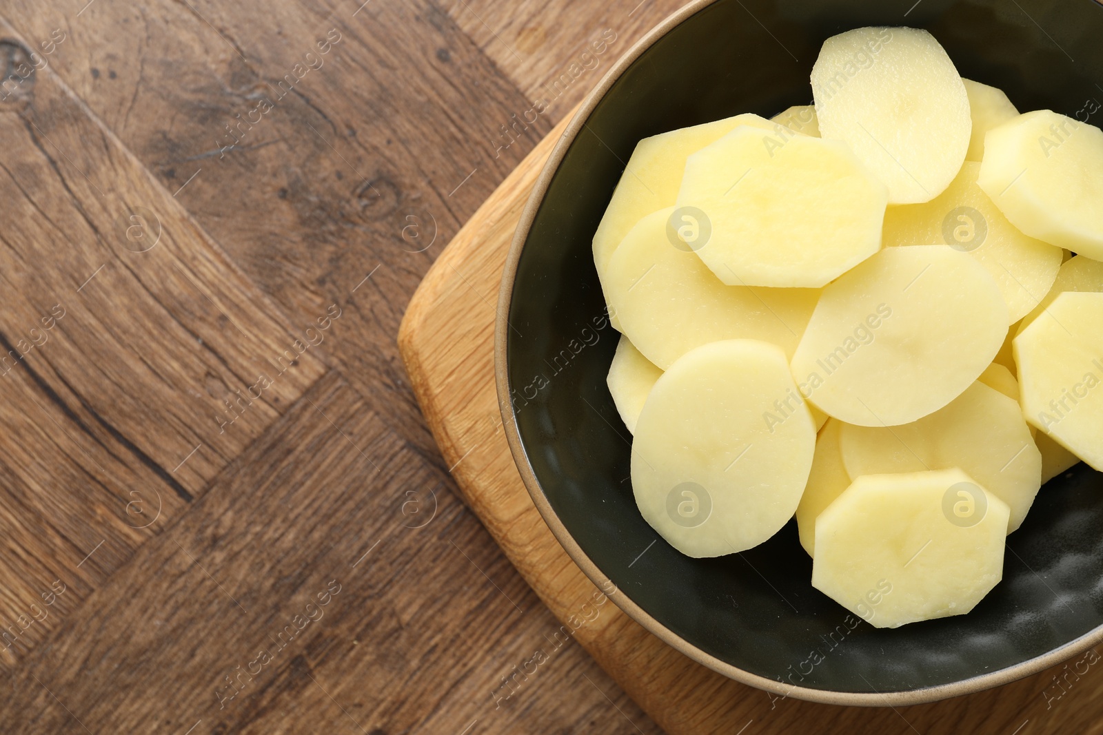 Photo of Cut fresh raw potatoes in bowl on wooden table, top view. Space for text