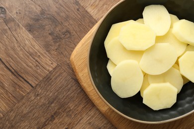 Cut fresh raw potatoes in bowl on wooden table, top view. Space for text