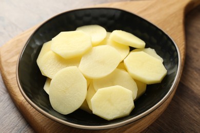 Photo of Cut fresh raw potatoes in bowl on wooden table