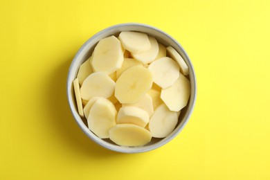 Photo of Cut fresh raw potatoes in bowl on yellow background, top view