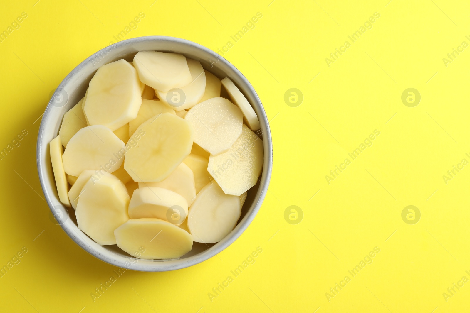 Photo of Cut fresh raw potatoes in bowl on yellow background, top view. Space for text