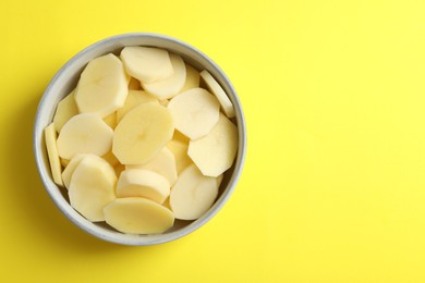 Cut fresh raw potatoes in bowl on yellow background, top view. Space for text