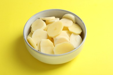 Photo of Cut fresh raw potatoes in bowl on yellow background