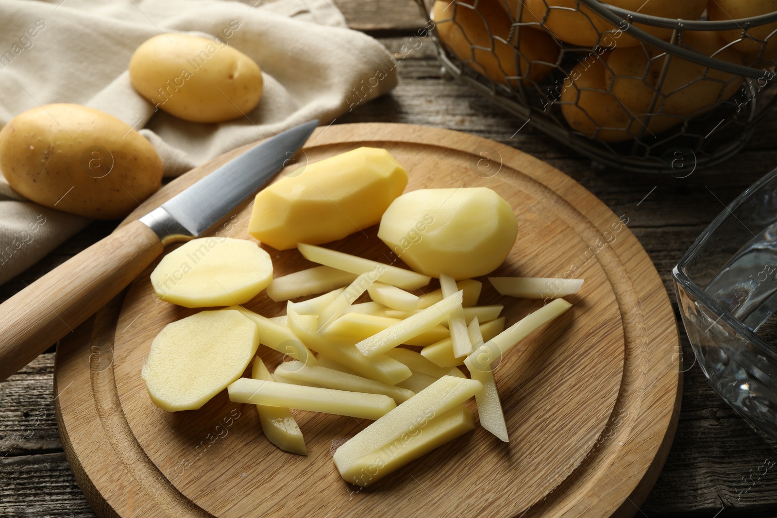 Photo of Whole and cut fresh raw potatoes near knife on wooden table