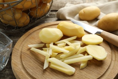 Photo of Whole and cut fresh raw potatoes near knife on wooden table