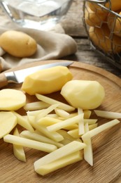 Photo of Whole and cut fresh raw potatoes near knife on wooden table