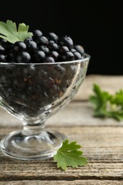 Ripe black currants and leaves in glass dessert bowl on wooden table, closeup