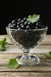 Photo of Ripe black currants and leaves in glass dessert bowl on wooden table