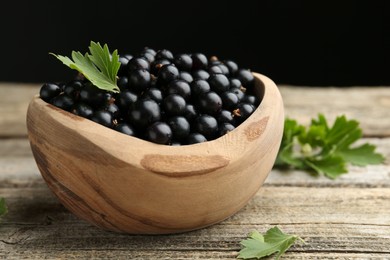 Photo of Ripe black currants and leaves in bowl on wooden table, closeup