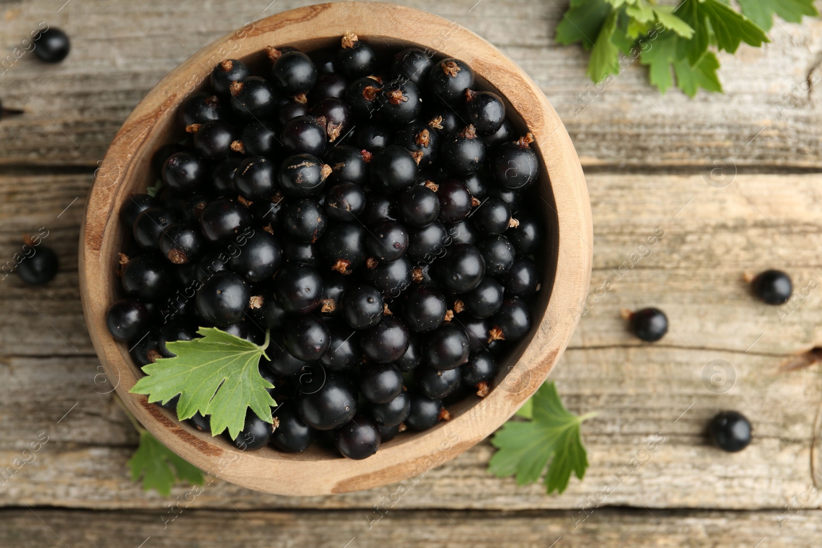 Photo of Ripe black currants and leaves in bowl on wooden table, top view