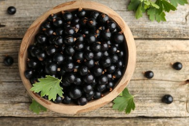 Ripe black currants and leaves in bowl on wooden table, top view