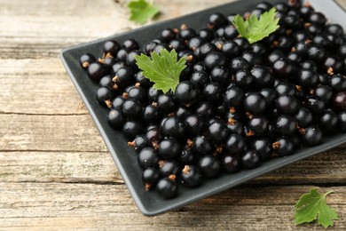 Ripe black currants and leaves on wooden table, closeup