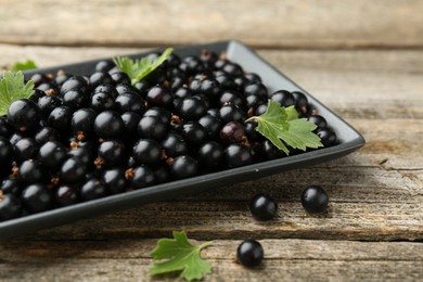 Photo of Ripe black currants and leaves on wooden table, closeup