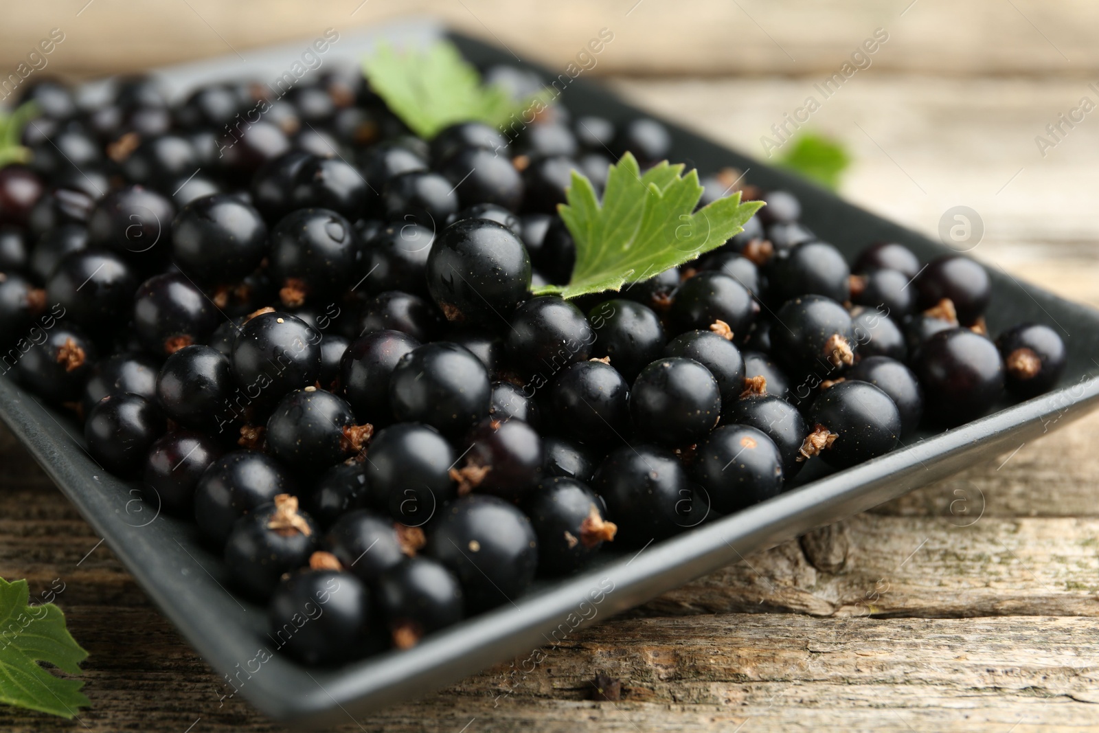 Photo of Ripe black currants and leaves on wooden table, closeup