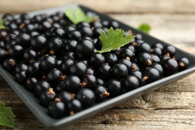 Photo of Ripe black currants and leaves on wooden table, closeup