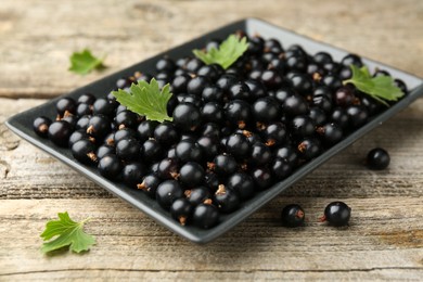 Photo of Ripe black currants and leaves on wooden table, closeup