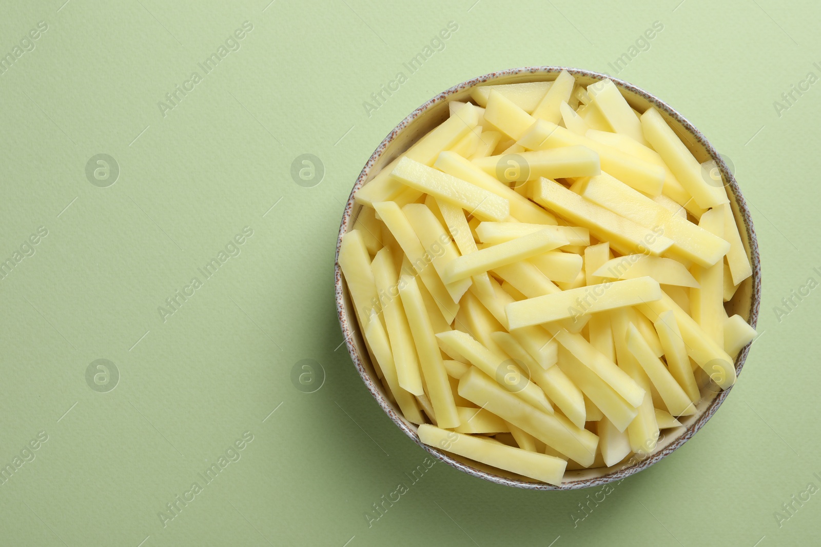 Photo of Fresh raw potatoes in bowl on green background, top view. Space for text