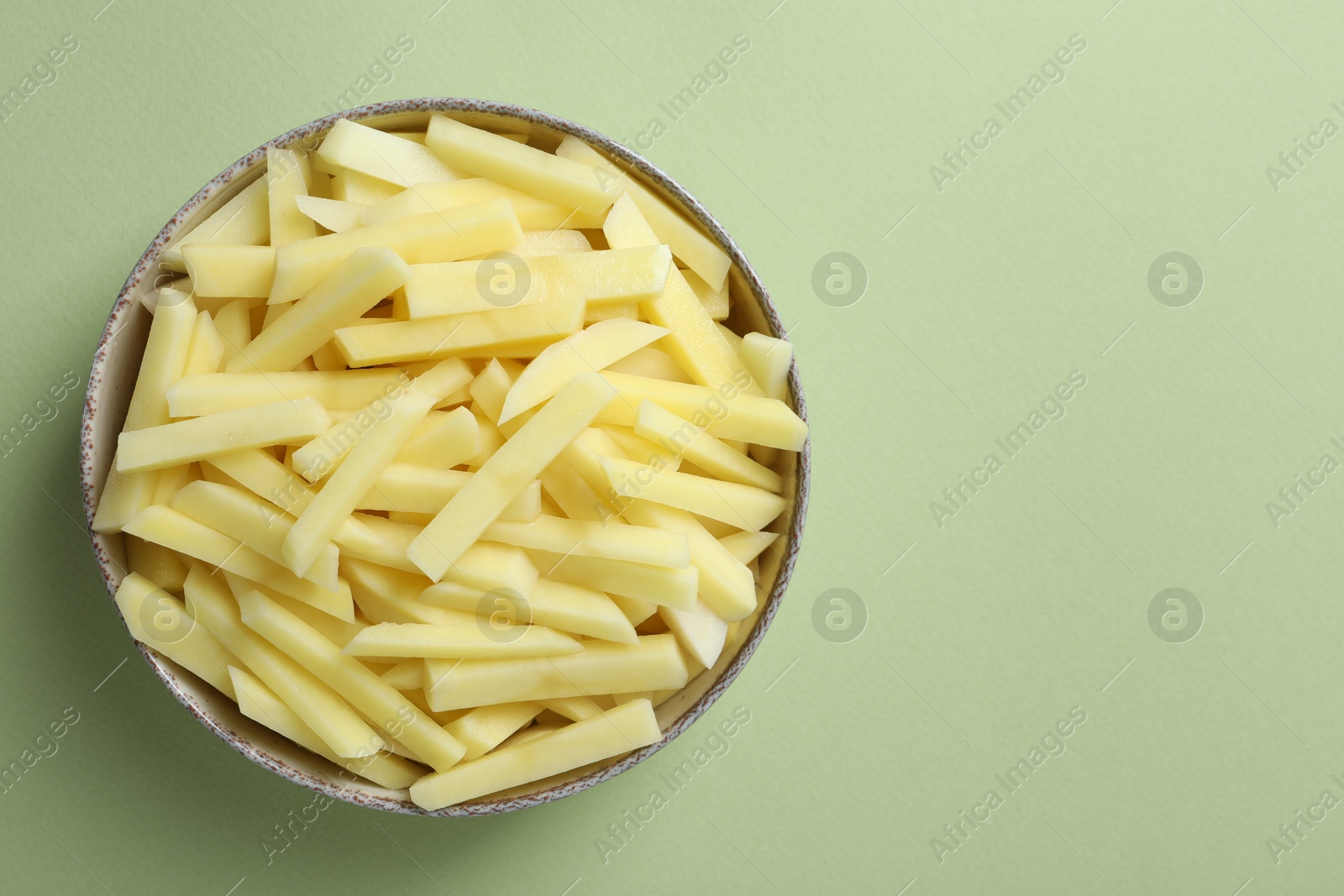 Photo of Fresh raw potatoes in bowl on green background, top view. Space for text