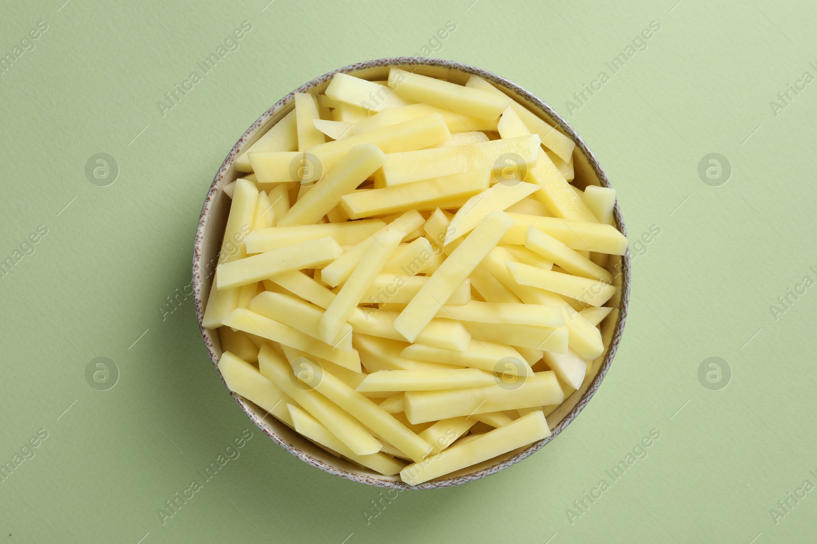 Photo of Fresh raw potatoes in bowl on green background, top view