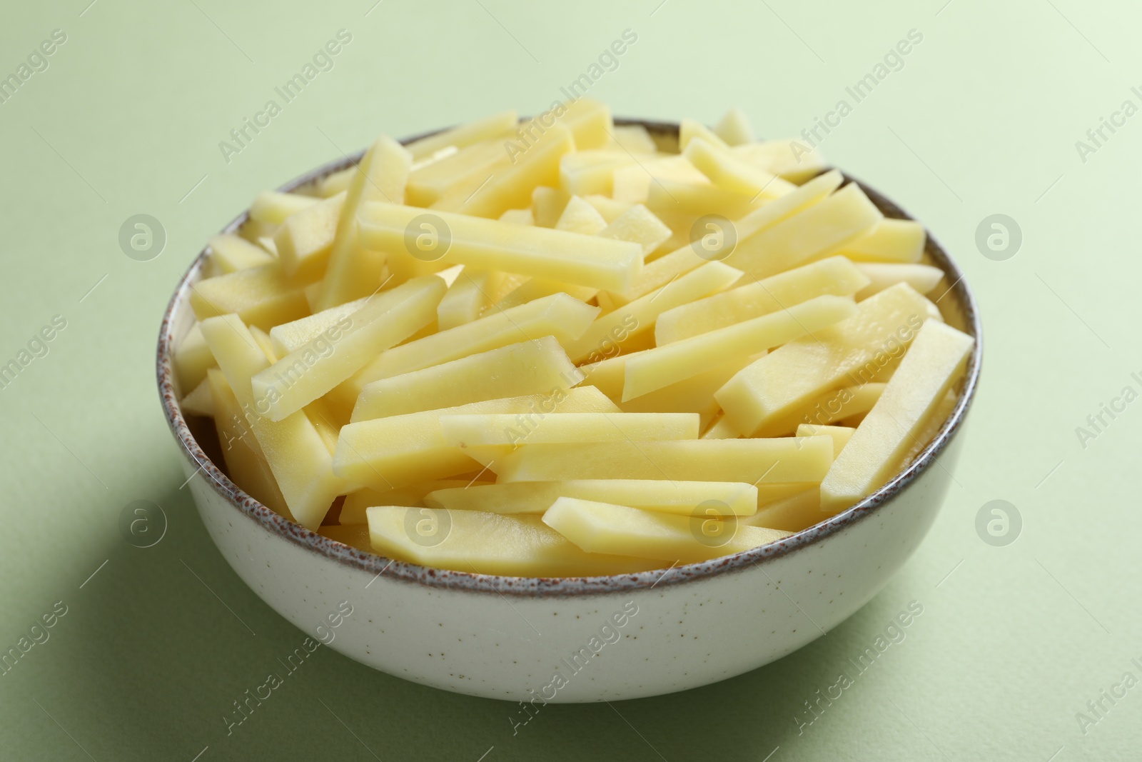 Photo of Fresh raw potatoes in bowl on green background