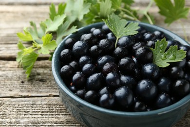 Ripe blackcurrants in bowl and green leaves on wooden table, closeup