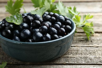 Ripe blackcurrants in bowl and green leaves on wooden table, closeup