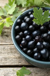 Ripe blackcurrants in bowl and green leaves on wooden table