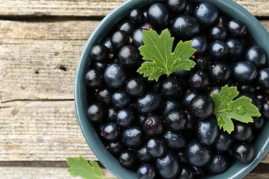 Ripe blackcurrants in bowl and green leaves on wooden table, top view