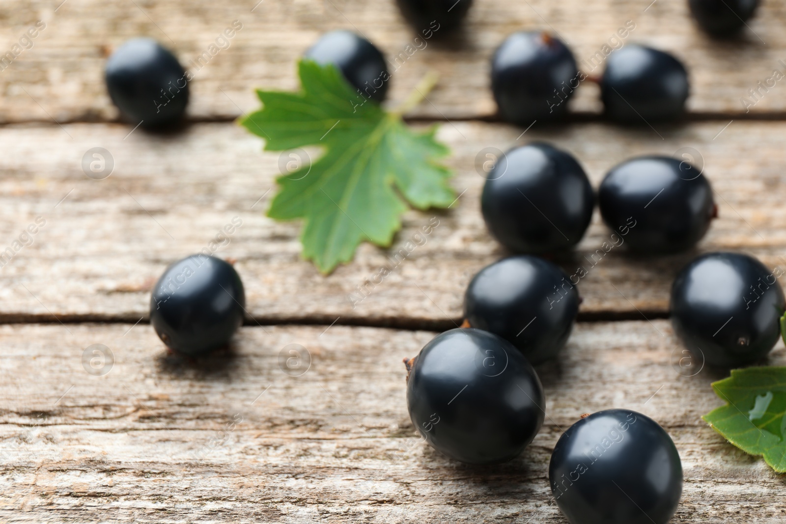 Photo of Ripe blackcurrants and green leaves on wooden table, closeup