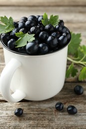 Ripe blackcurrants in mug and green leaves on wooden table