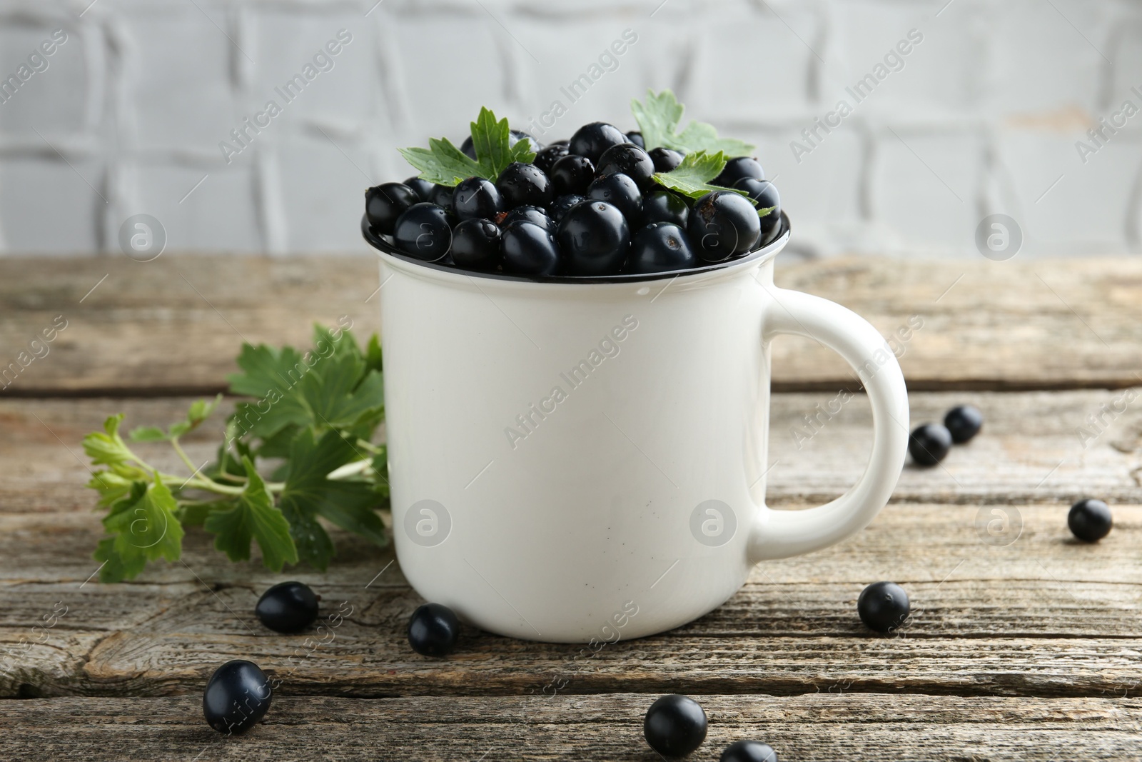 Photo of Ripe blackcurrants in mug and green leaves on wooden table