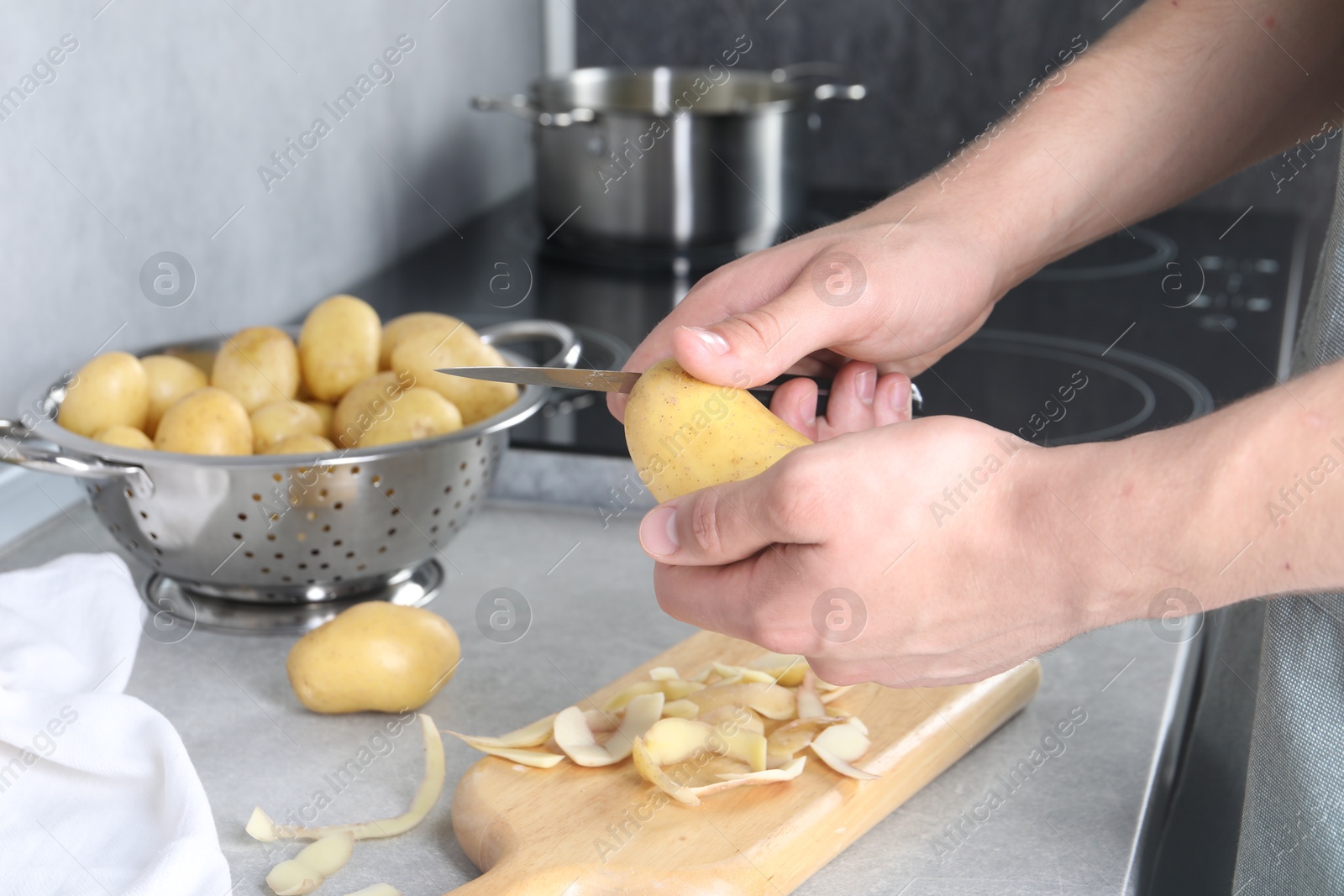 Photo of Man peeling fresh potato at grey countertop in kitchen, closeup