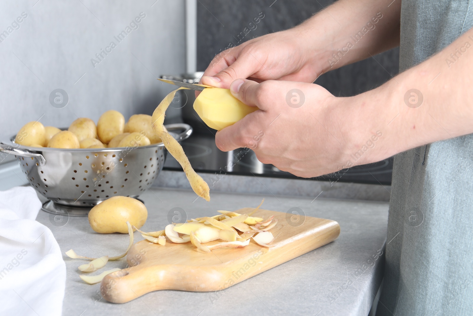 Photo of Man peeling fresh potato at grey countertop in kitchen, closeup