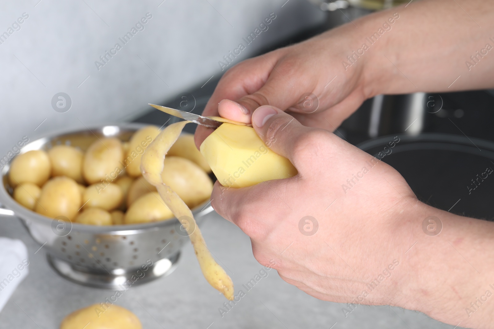 Photo of Man peeling fresh potato at grey countertop in kitchen, closeup