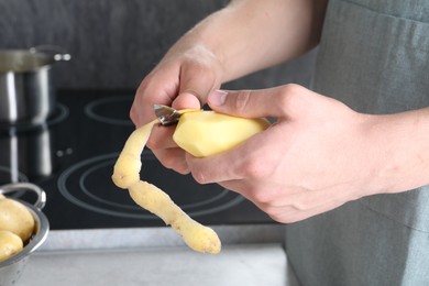 Photo of Man peeling fresh potato at grey countertop in kitchen, closeup