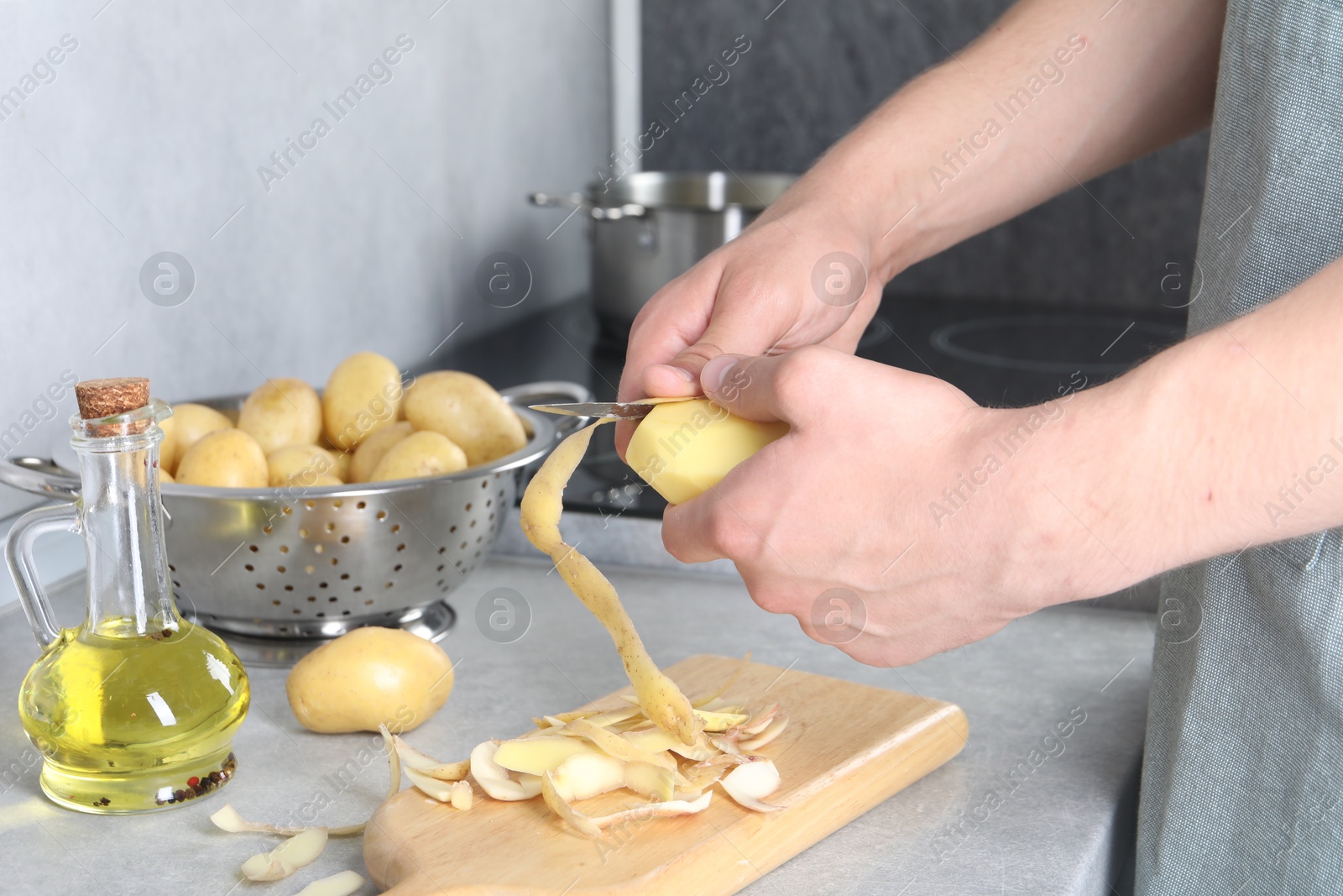 Photo of Man peeling fresh potato at grey countertop in kitchen, closeup