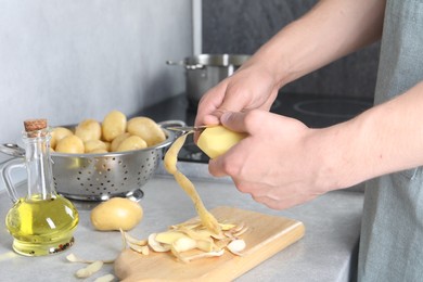 Man peeling fresh potato at grey countertop in kitchen, closeup