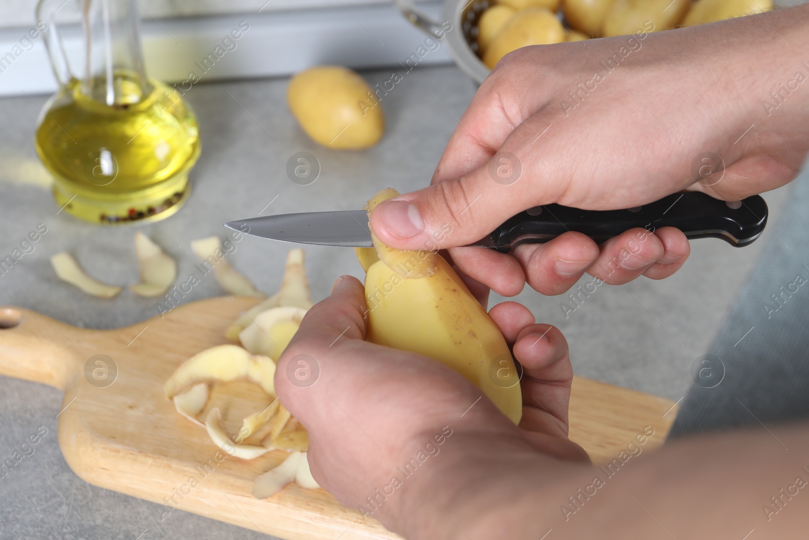 Photo of Man peeling fresh potato at grey countertop in kitchen, closeup