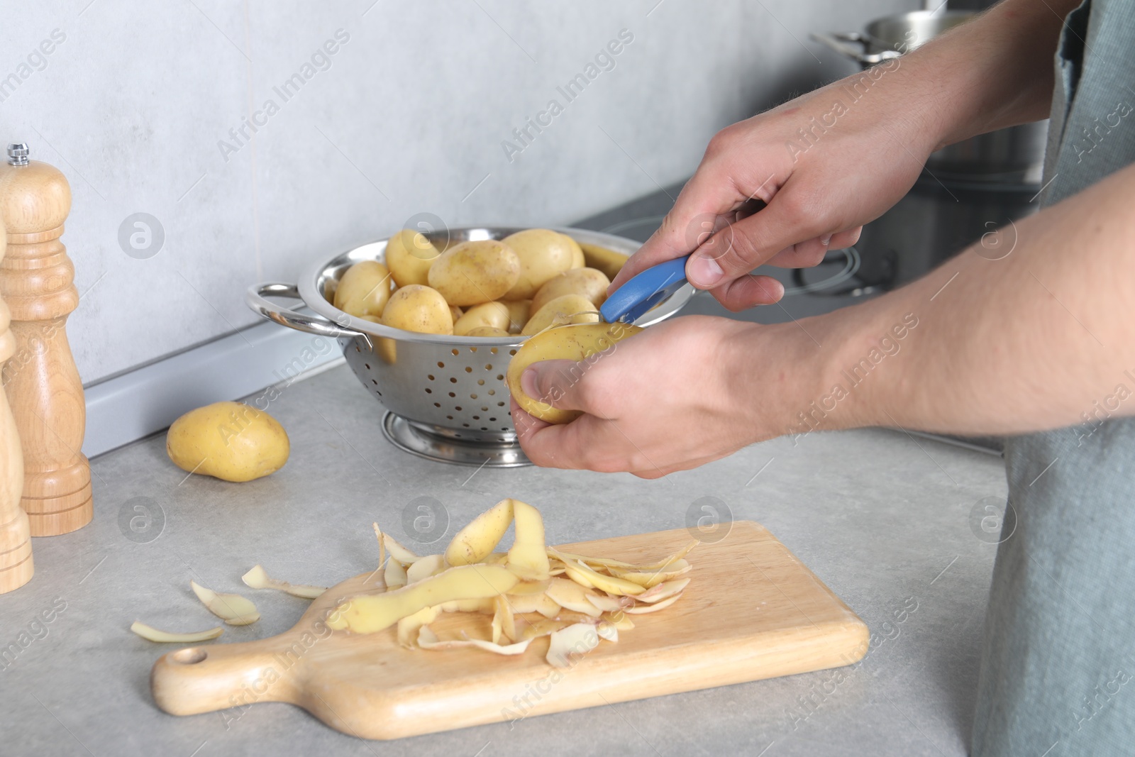 Photo of Man peeling fresh potato at grey countertop in kitchen, closeup