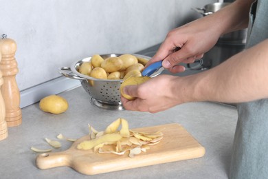 Man peeling fresh potato at grey countertop in kitchen, closeup