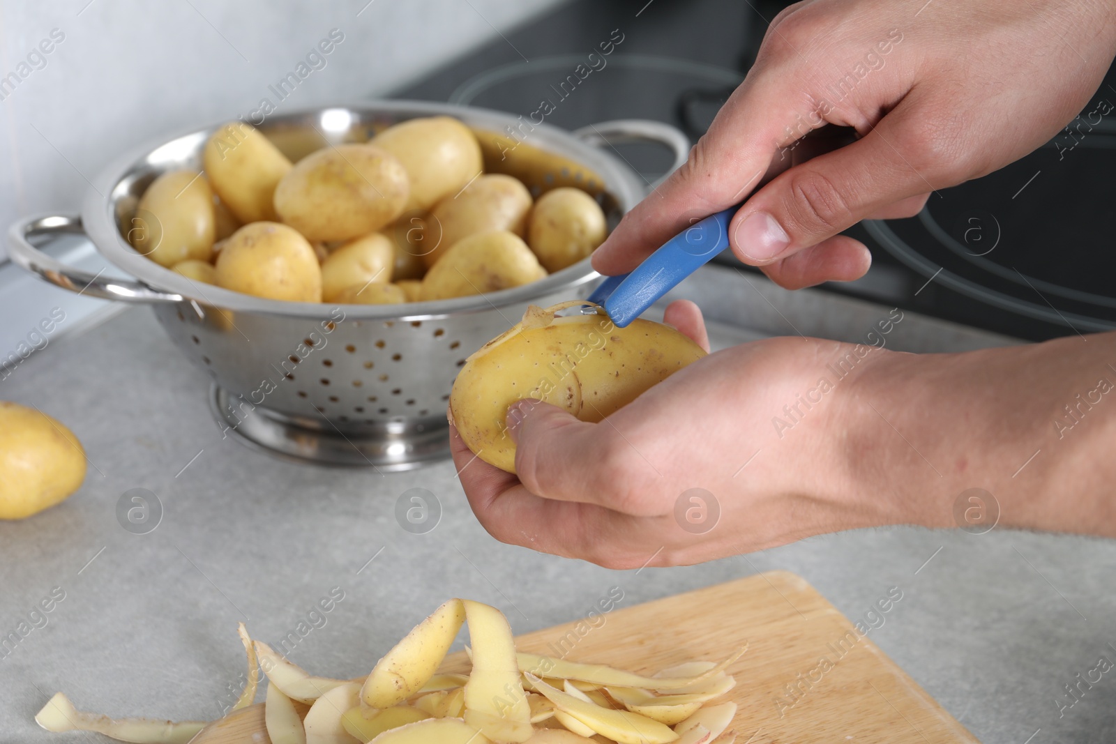 Photo of Man peeling fresh potato at grey countertop in kitchen, closeup