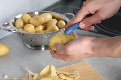 Man peeling fresh potato at grey countertop in kitchen, closeup